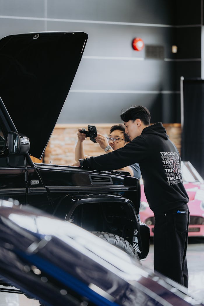 Two men examine a car engine in a modern workshop, focusing on repair and maintenance tasks.