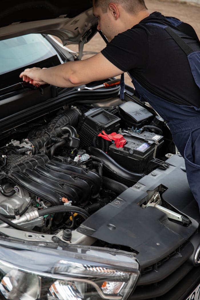 Mechanic in overalls fixing a car engine, focusing on maintenance and repair outdoors.